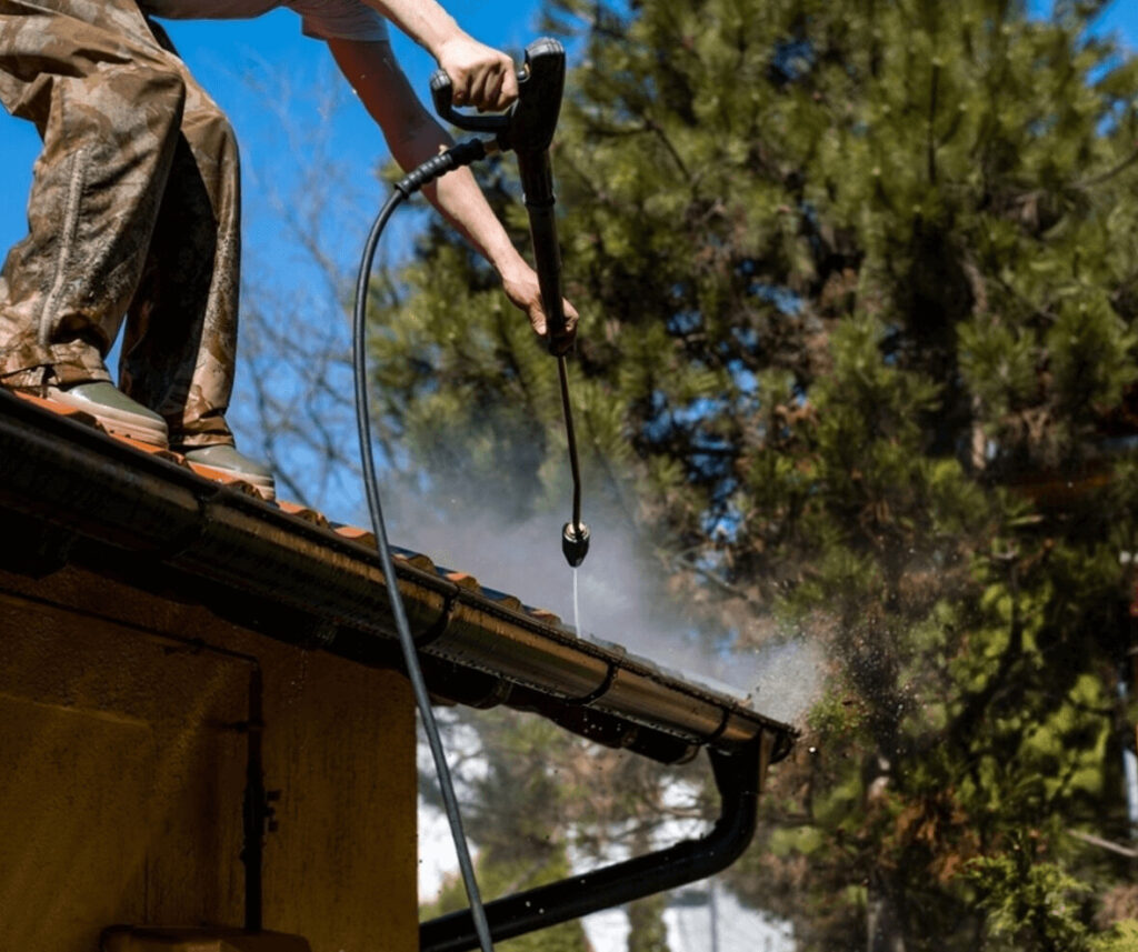A plumber adjusting tiles near a gutter system on a residential property.